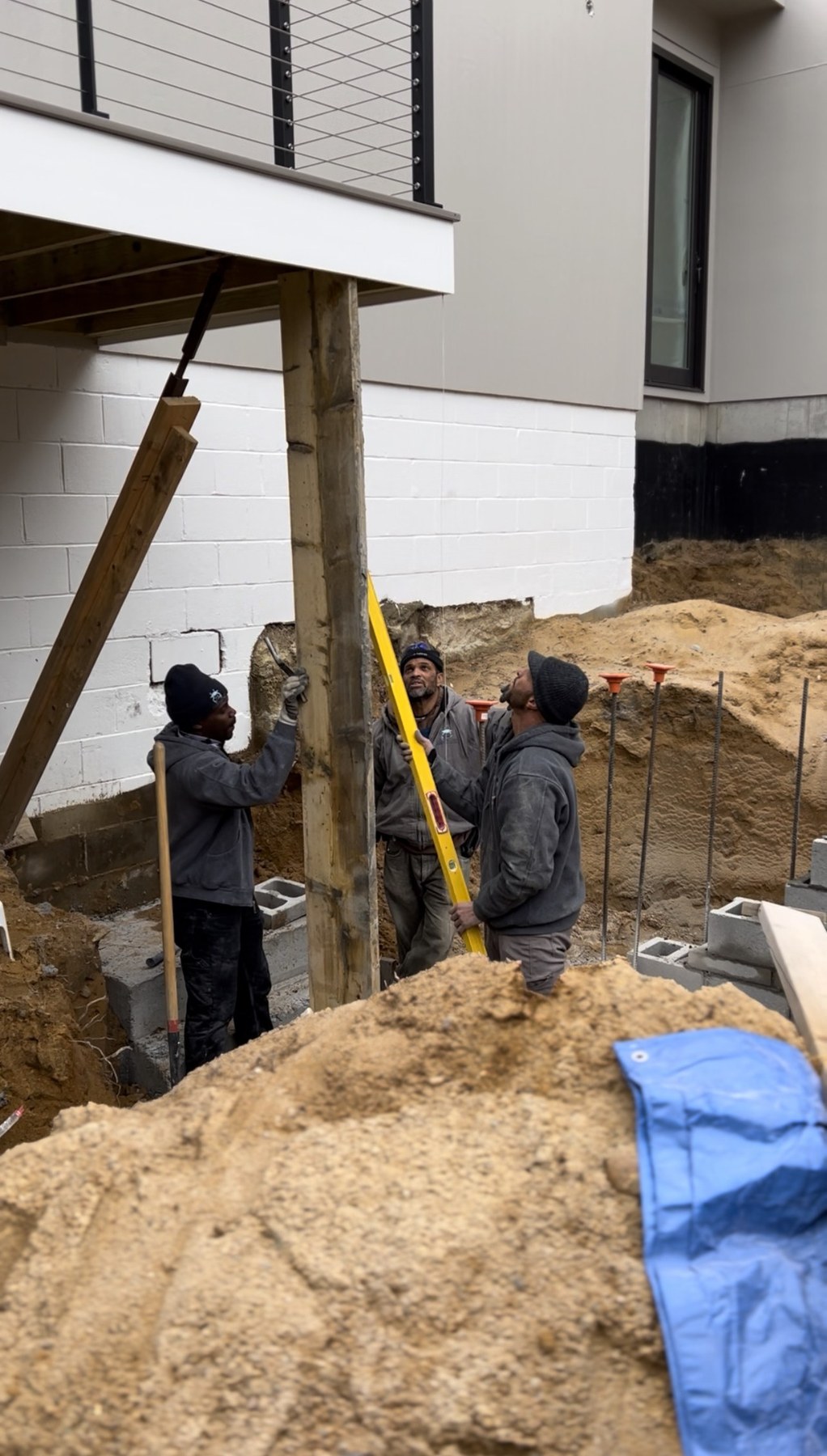 Three Blue Claw Associates crew members leveling a structural post on a foundation excavation, working together in a hardscape build