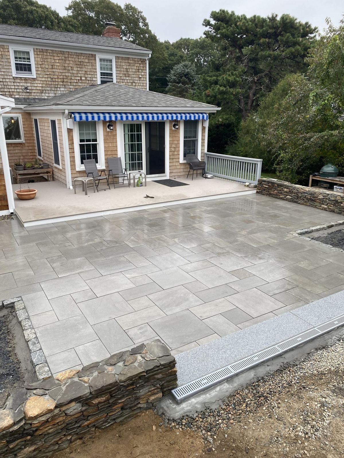 Thermal bluestone patio with a granite curb step at the back of a shingled Cape home