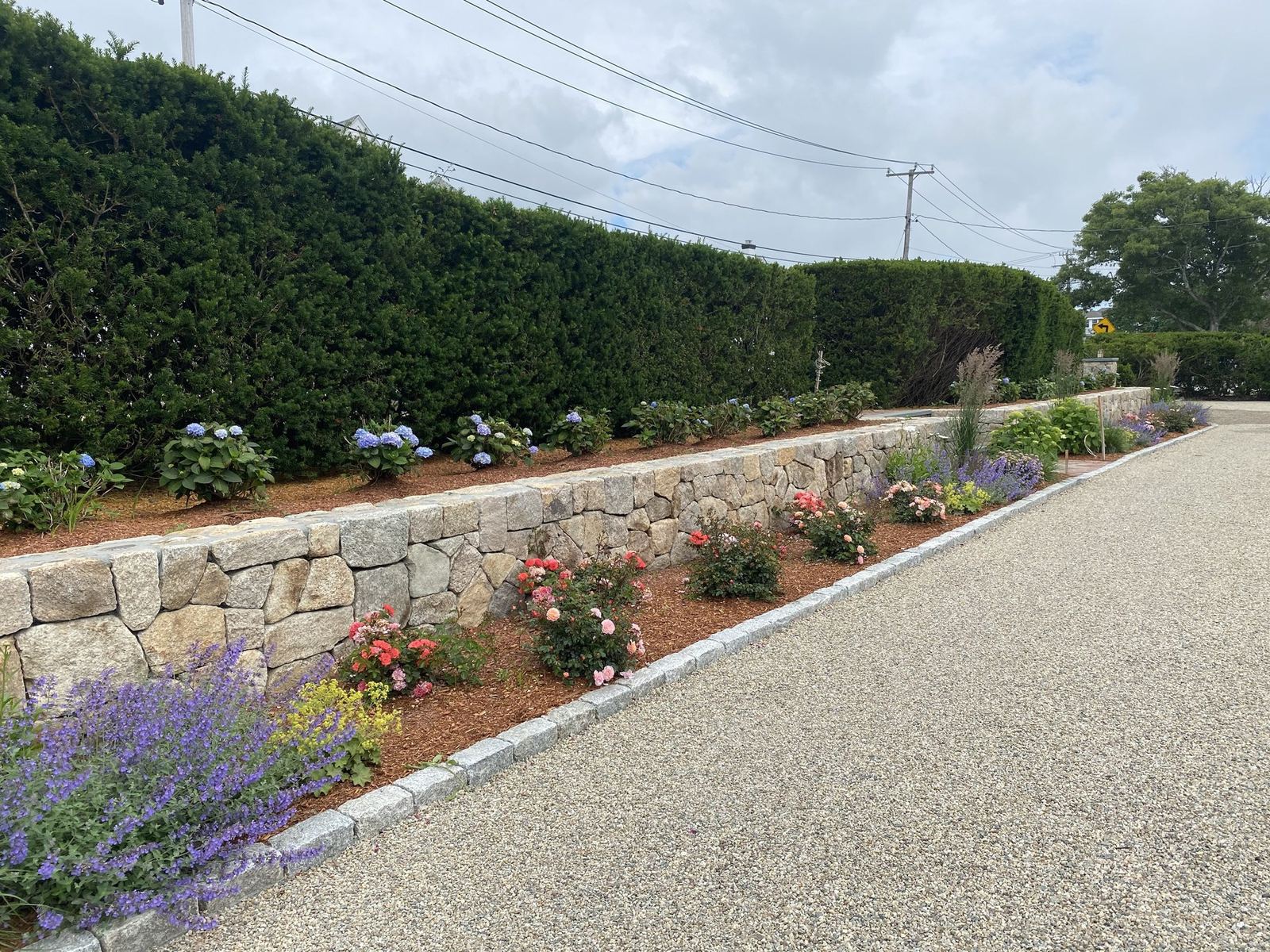 Hand-set fieldstone wall retaining a planted bed along a pea-stone drive